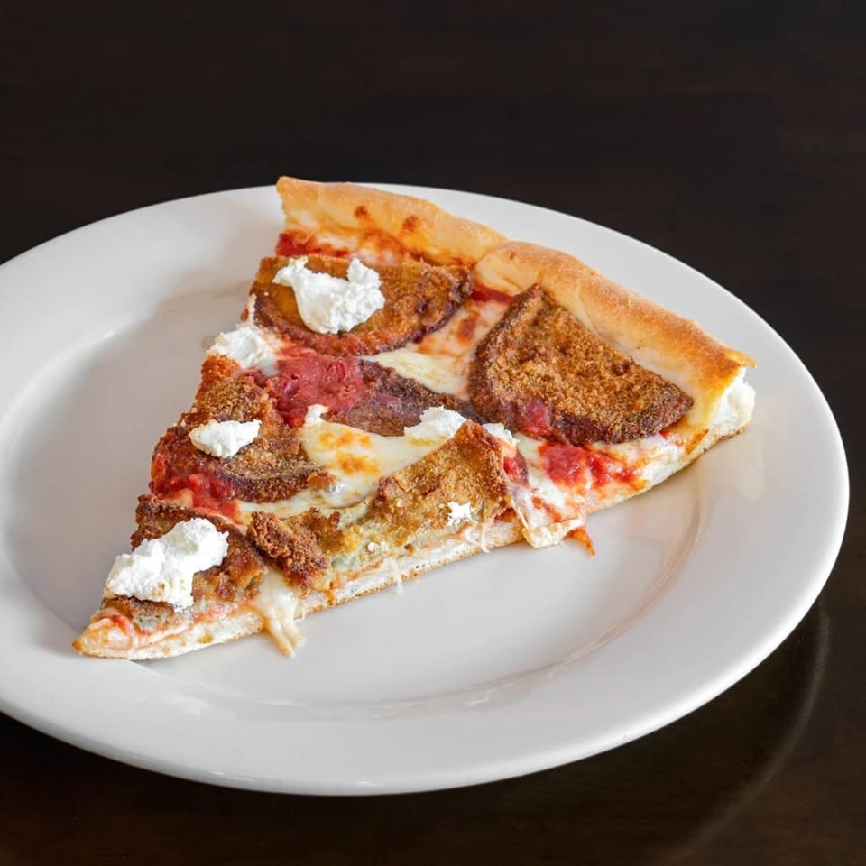 A slice of Franco's Pizza with breaded eggplant, tomato sauce, mozzarella, and ricotta cheese.