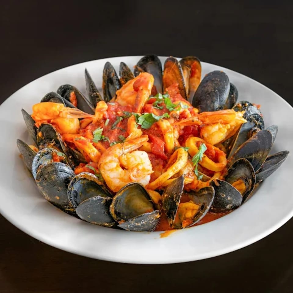 A white bowl filled with mussels, shrimp, and calamari in a rich red tomato sauce.