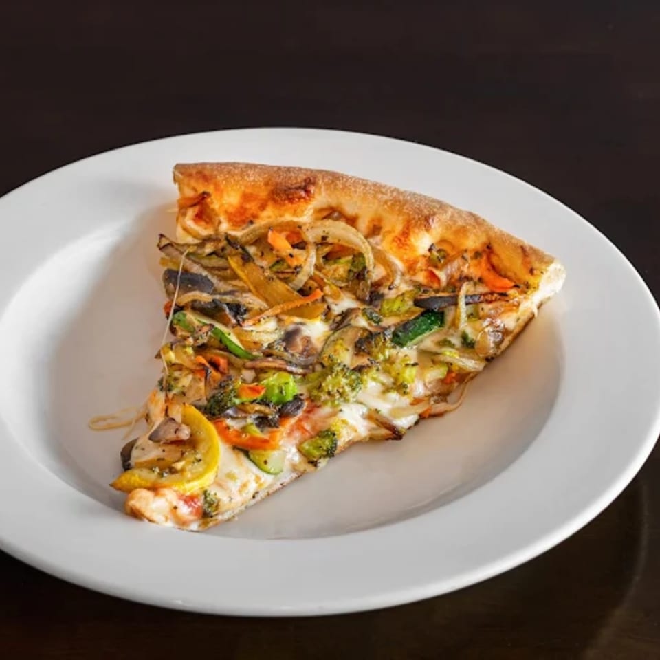 A single slice of Franco's Pizza with various vegetables and melted cheese on a white plate.