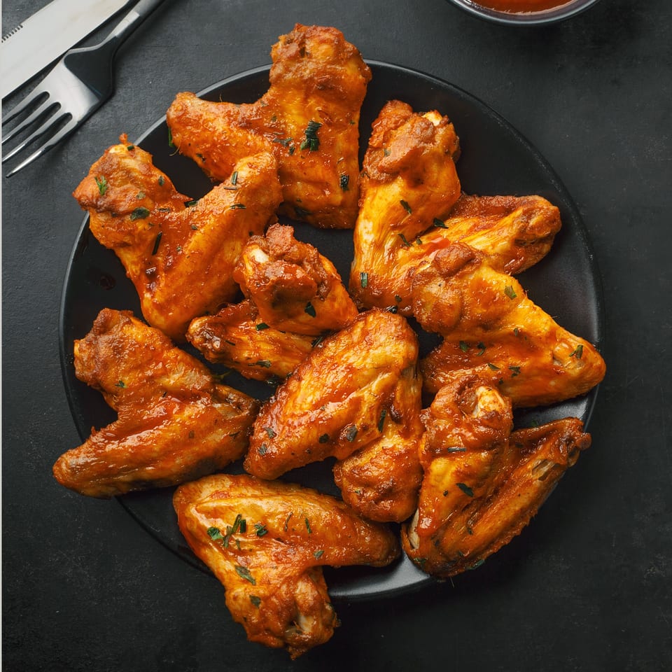 A black plate filled with Franco's Pizza's buffalo chicken wings, garnished with herbs.