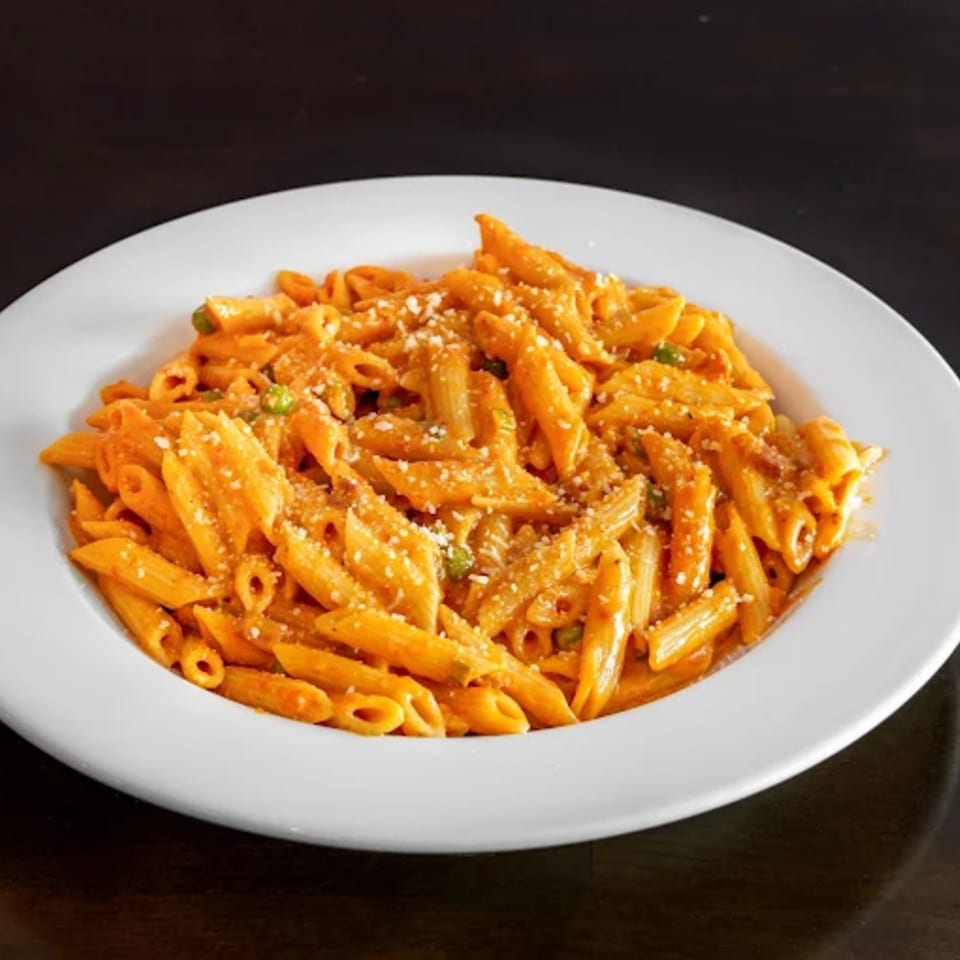 A white plate filled with penne pasta in a creamy orange sauce, topped with grated cheese.